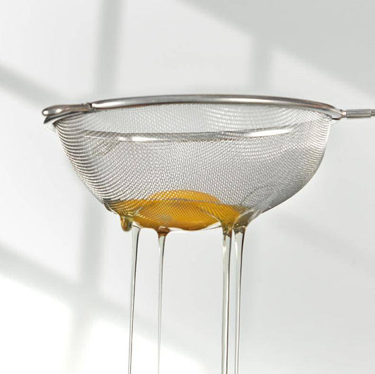Double Ear Food Strainer 20CM filtering egg whites with fine mesh, showcasing its precision and control for delicate kitchen tasks.