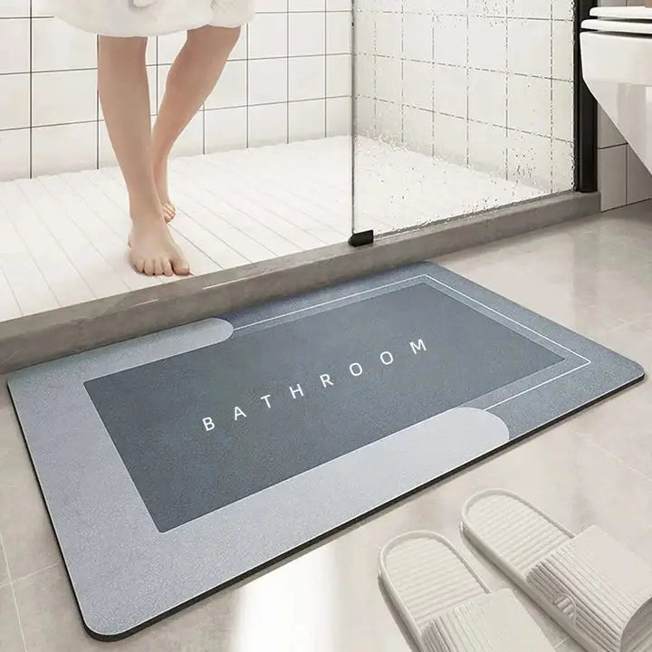 Rectangular floor mat with 'BATHROOM' text in light grey tones placed outside a shower. Absorbent mat keeps floors dry and safe.
