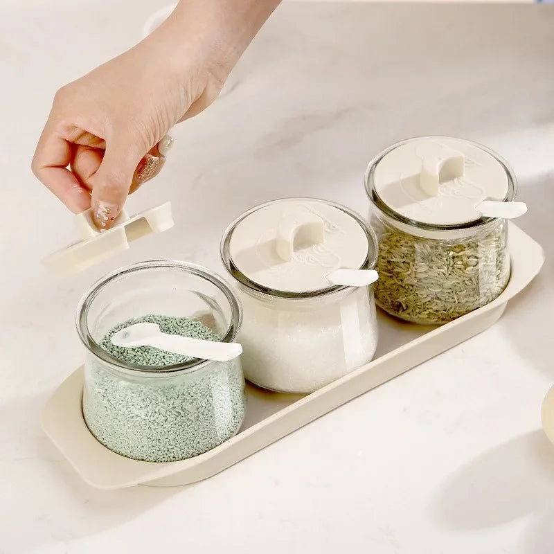 3PCS Glass Seasoning Storage Bottles Set with white lids and spoons on a beige tray, ideal for organizing spices in modern kitchens.