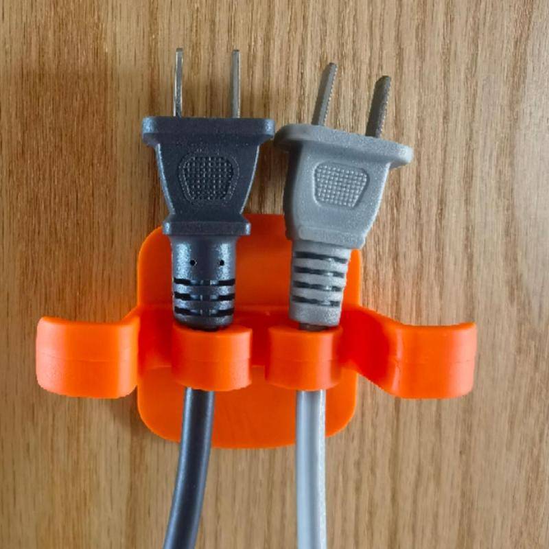 Orange Hole-Free Wire Holder mounted on wood, securing two power cords neatly for organized cable storage in home or office.