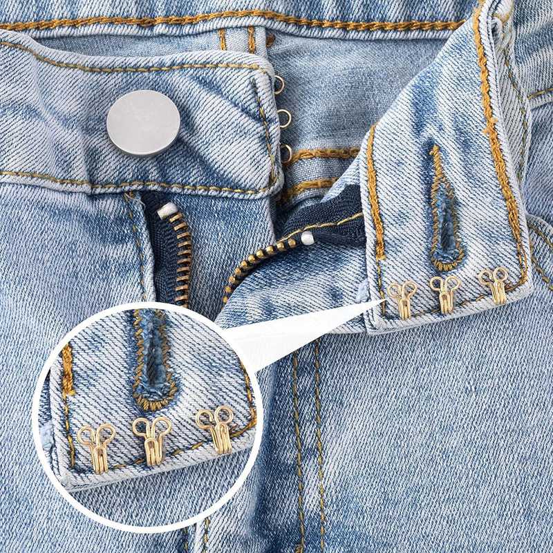 Close-up of brass sewing hooks & eye closures attached to denim jeans, demonstrating durable fastening for clothing repairs.