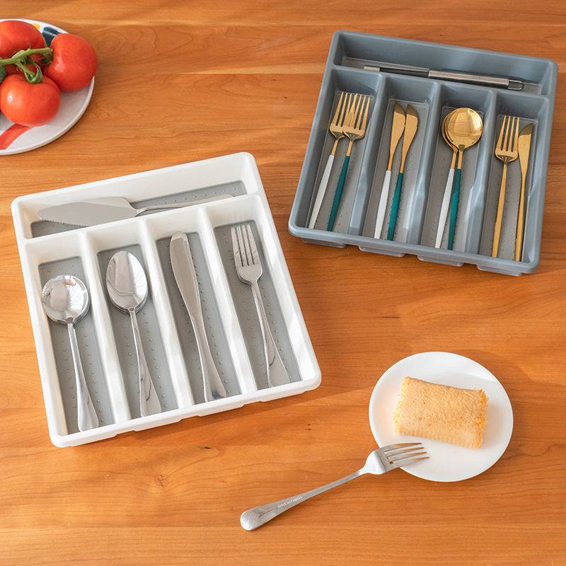 Durable 5 Grids Plastic Cutlery Tray in gray and white, shown with assorted utensils neatly organized on a wooden kitchen table.