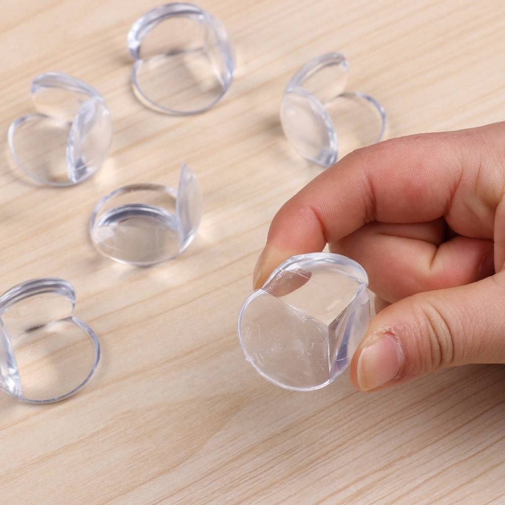 Silicone Table Corner Guard 4PCS shown on wooden surface with one piece held in hand, highlighting soft clear silicone and adhesive backing.