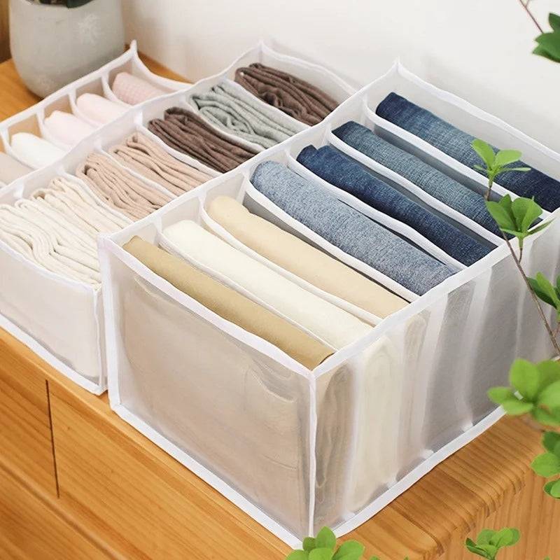 White 7-grid dresser drawer storage boxes neatly organizing jeans, trousers, and undergarments on a wooden surface for efficient closet use.