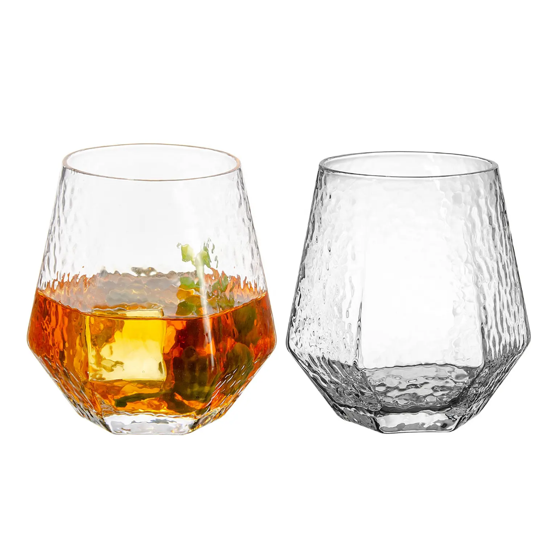 Close-up of two Hammered Diamond Whiskey Glasses, one with whiskey and ice, showcasing textured glass design for modern drinkware sets.