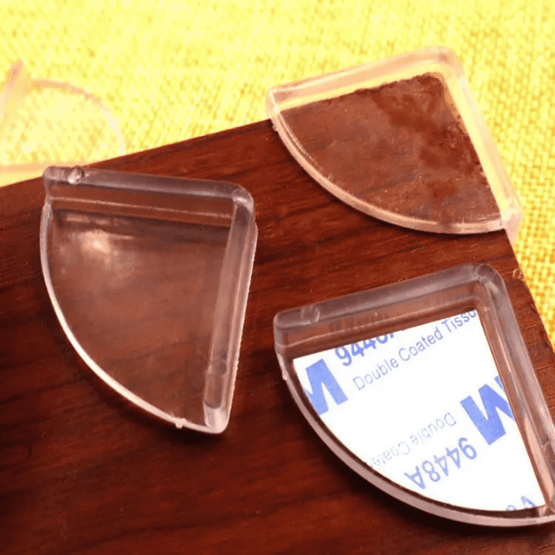 Close-up of transparent silicone Table Corner Protector Baby Safety 4 PCS with adhesive backing applied to wooden furniture corner.