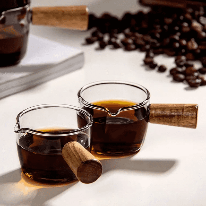 Glass Espresso Measuring Cup - 100 ml Measuring Cup with wooden handle, filled with espresso, ideal for precise brewing in home or café settings.