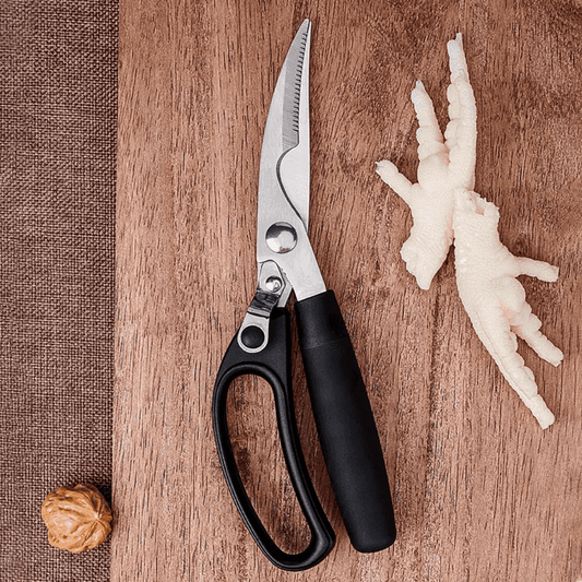 Multipurpose kitchen scissor placed on wooden board beside chicken feet, showcasing its use for poultry and food preparation tasks.