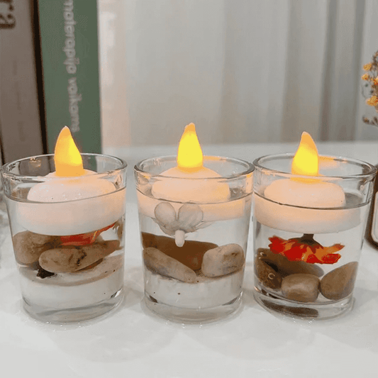 Set of 3 floating LED candles in clear glasses with stones and flowers, emitting warm light; ideal waterproof flameless decor for events or home.