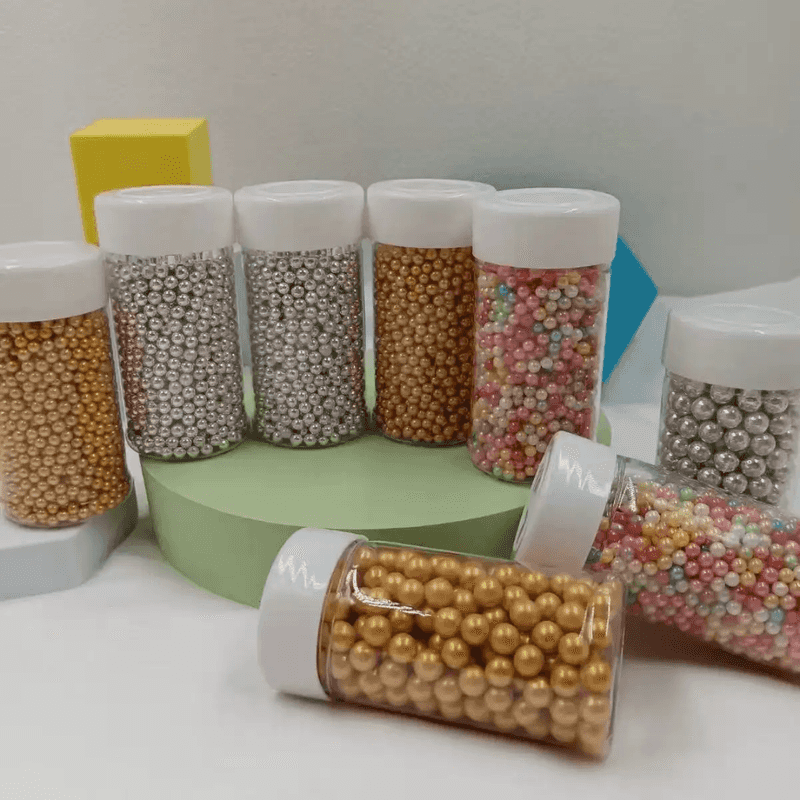 Assorted Edible Sugar Beads Cake Decoration 85g in clear plastic jars with white lids, ideal for decorating cakes and desserts.