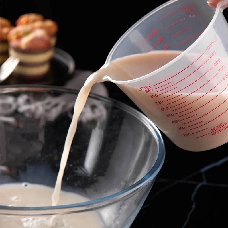 Durable 1000ml plastic measuring cup pouring liquid into bowl, clear design with red markings for accurate kitchen use.