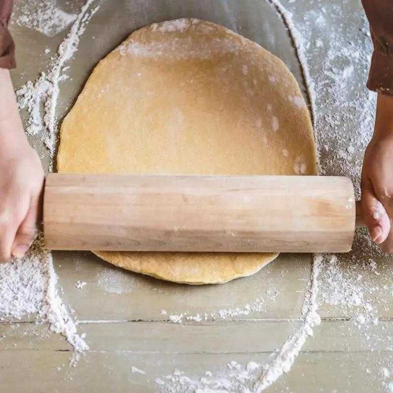 Handmade wooden rolling pin in use flattening dough on a floured surface. Perfect kitchen utensil for baking rotti or pizza at home.
