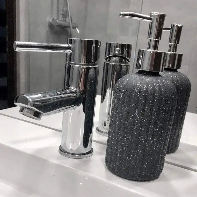Marble Black Glass Soap Dispenser 450 ml placed beside a chrome faucet on a bathroom sink, enhancing room essentials with luxury bath accessories.