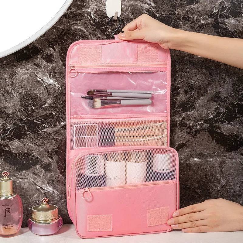 Pink foldable makeup bag hanging open with organized compartments for brushes and bottles. Stylish toiletry bag for travel and daily beauty storage.