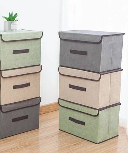 Stacked foldable cloth storage boxes with lids in green, beige, and grey, designed for efficient closet organization and space-saving.
