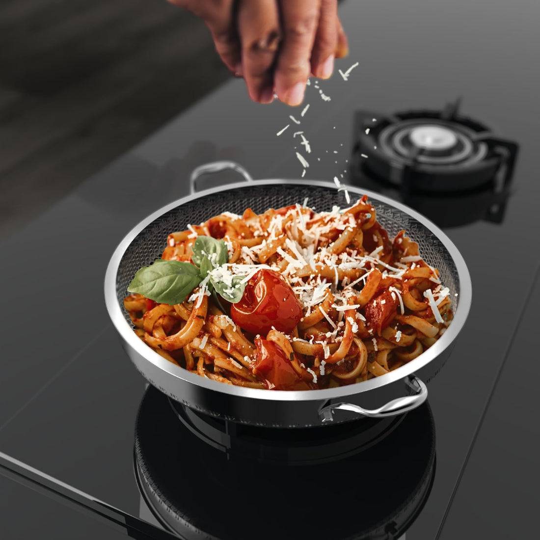 Stainless steel non-stick frying pan with two handles, featuring a scratch-resistant surface, used for cooking pasta with fresh ingredients on a gas stove.