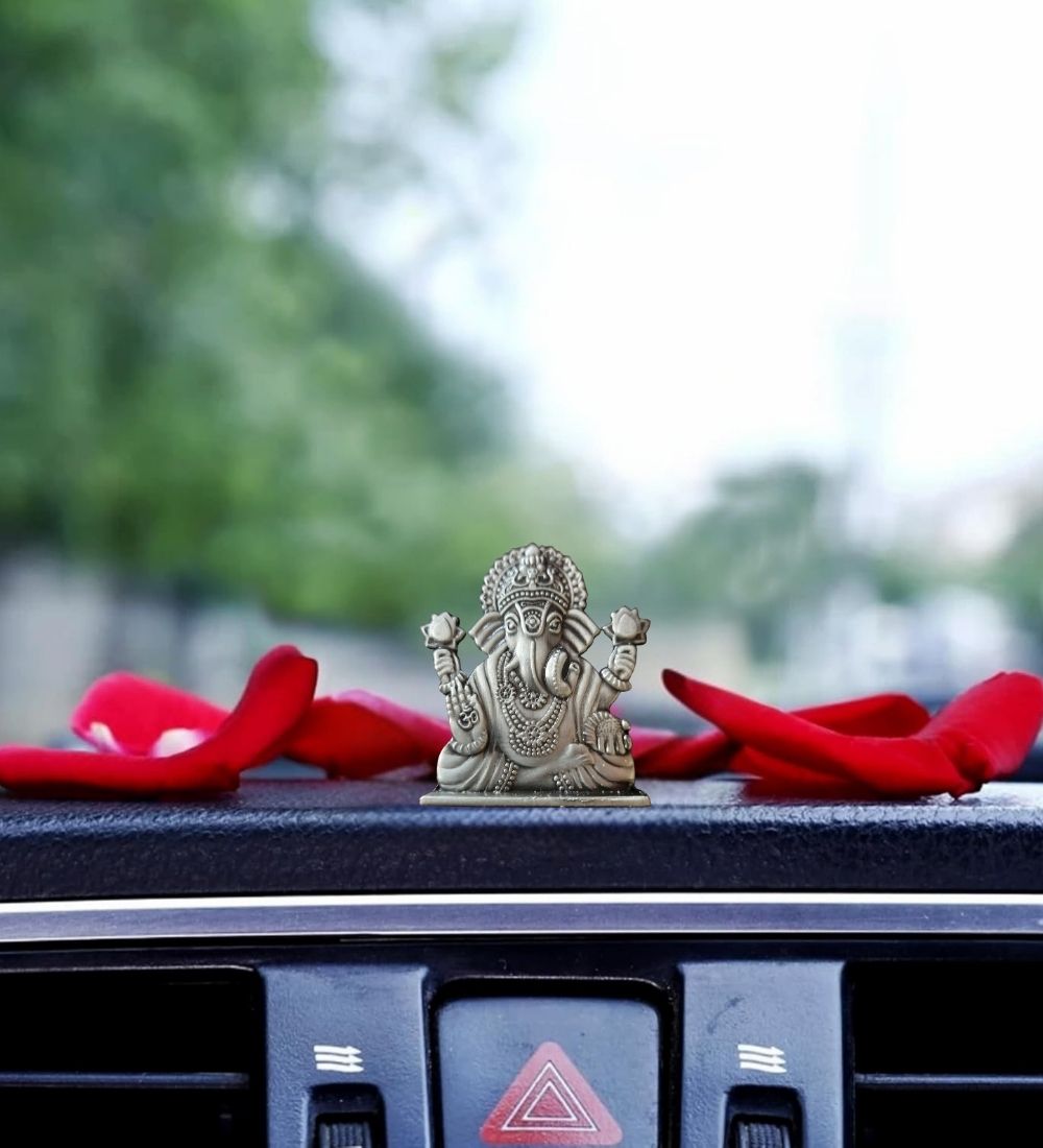 Ganesha Idol For Car Dashboard placed on a car interior with red petals, combining spiritual charm and elegant dashboard accessory.