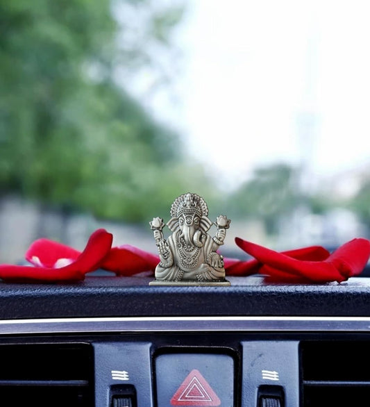 Ganesha Idol For Car Dashboard placed on a car interior with red petals, combining spiritual charm and elegant dashboard accessory.