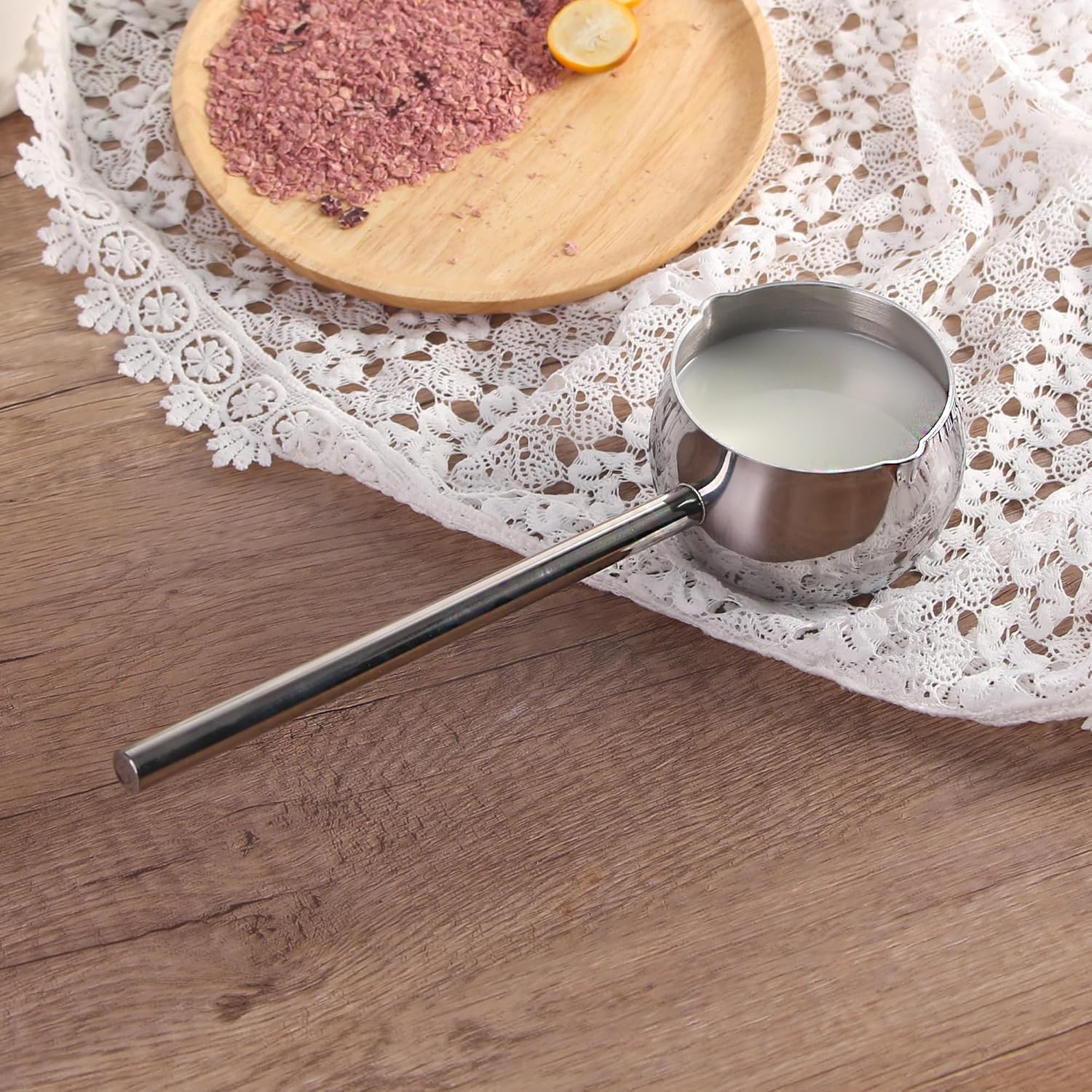 Mini Stainless Steel Measuring Melting Pot | Bamagate.com placed on a wooden surface with milk inside, featuring a long handle and dual spouts for easy pouring.
