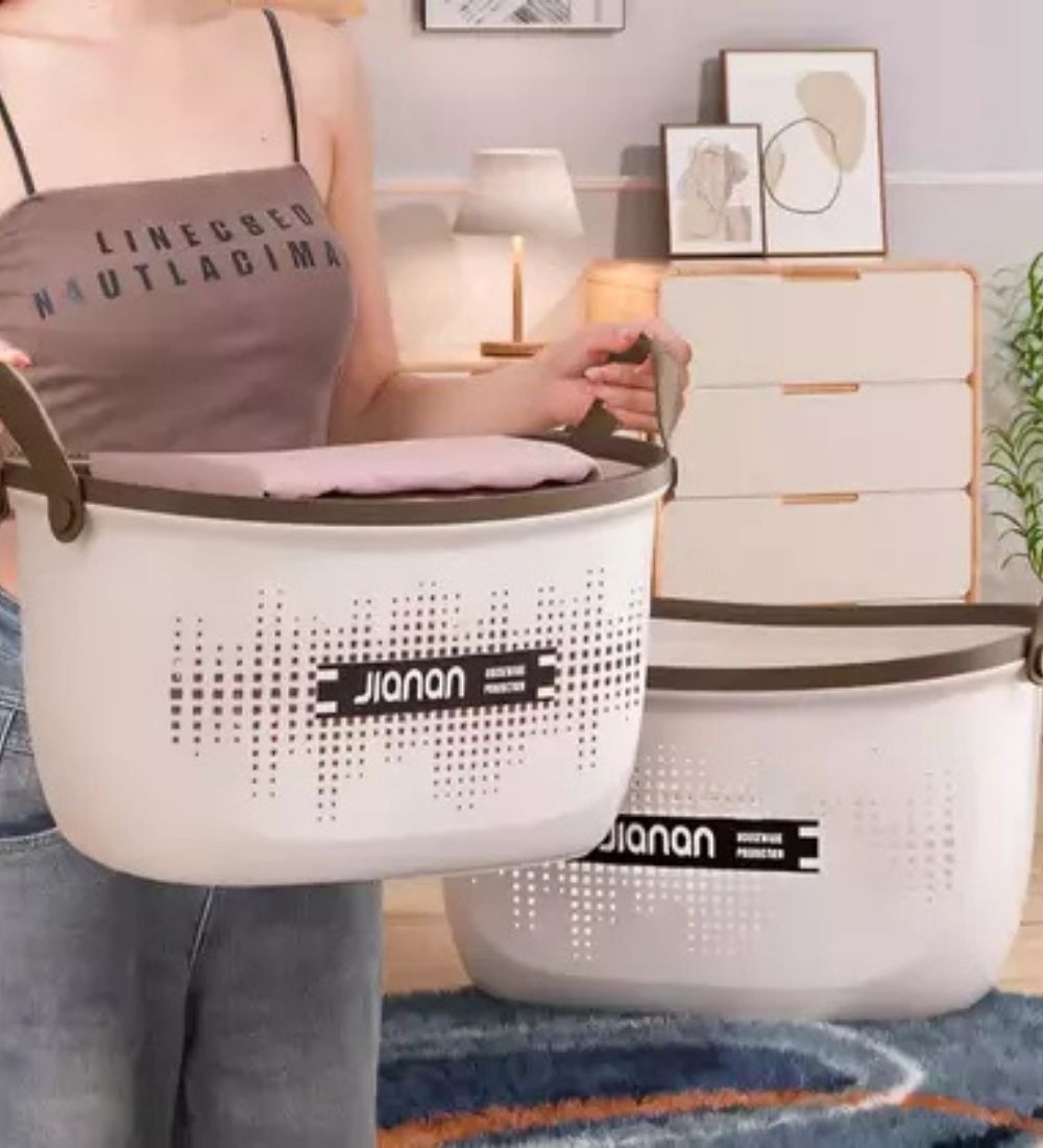 Person holding Multipurpose Plastic Basket with Handle, showcasing its use for laundry and home organization in a modern interior setting.