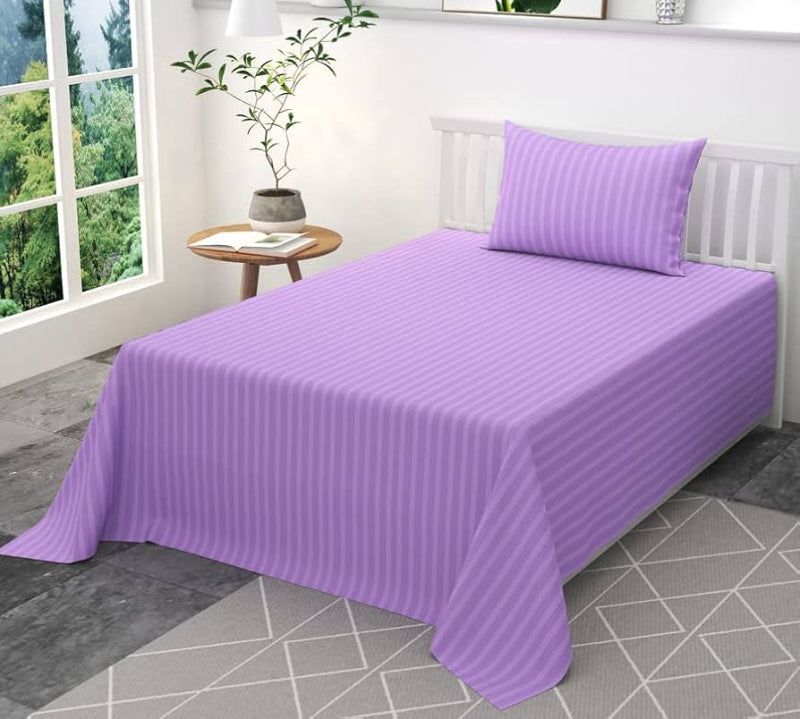 Purple bedspread and pillow on a bed in a bright room with a plant and small table.