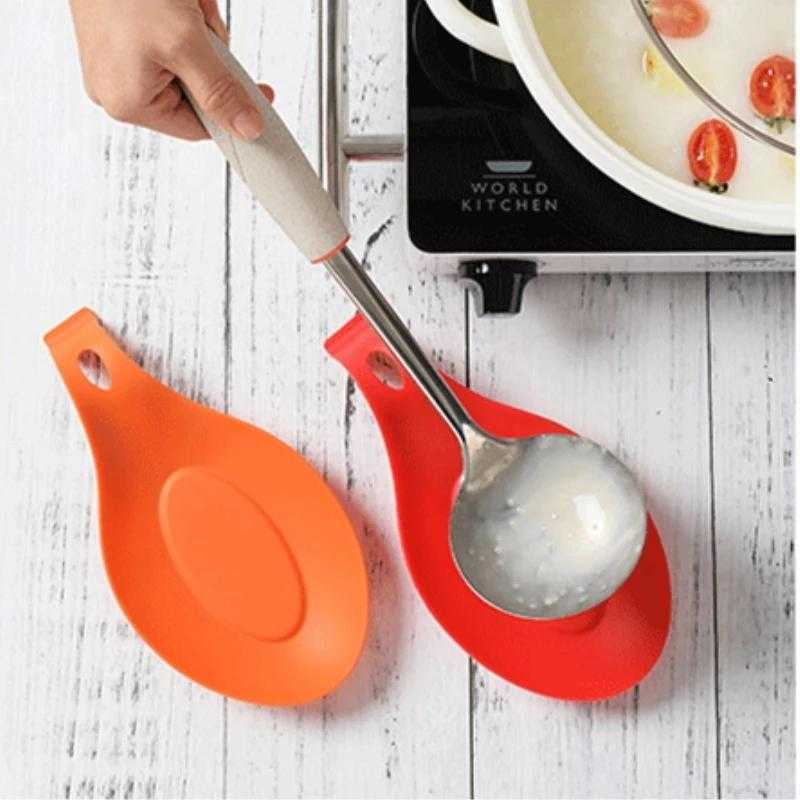 Red and orange Silicone Spoon Rest Pads placed near a stove, holding a soup ladle. Heat-resistant and hygienic kitchen accessory.